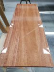Hardwood panel finished with a smooth clear coat to enhance natural grain and tone. Hardwood panel with a clear satin finish highlighting natural grain and color, curing in a professional wood finishing shop.