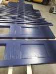 Custom cabinet doors and trim finished in a deep navy blue and staged for curing. Navy blue painted cabinet doors and matching trim pieces laid out for curing inside a professional finishing shop.