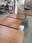 Custom solid wood tabletops finished and curing before final inspection. Multiple solid wood tabletops with smooth stained finishes curing on racks inside a professional wood finishing shop.